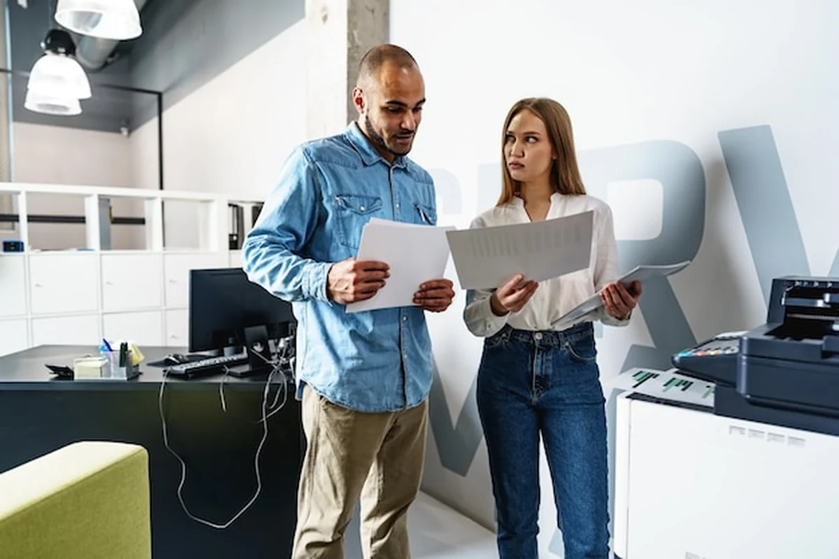 Dwaj pracownicy korzystają z nowoczesnej drukarki w biurze